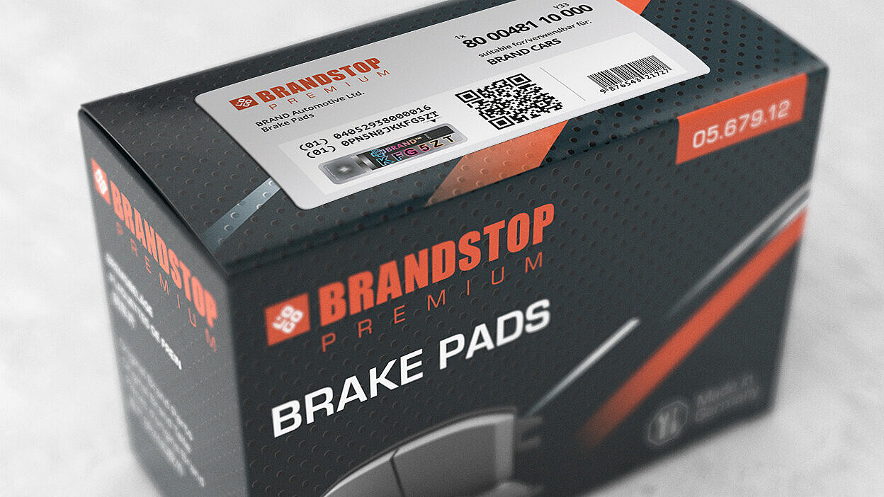 一个装有Brandstop高级刹车片的矩形盒子，表面贴有防伪标签。标签上印有二维码、产品信息以及独特的防伪元素，在激光光刻VeoMark®品牌下，全息设计展示了彩色字母数字字符（KFG5ZT）。该标签展示了先进的防伪技术，结合了公开和隐蔽的安全功能。